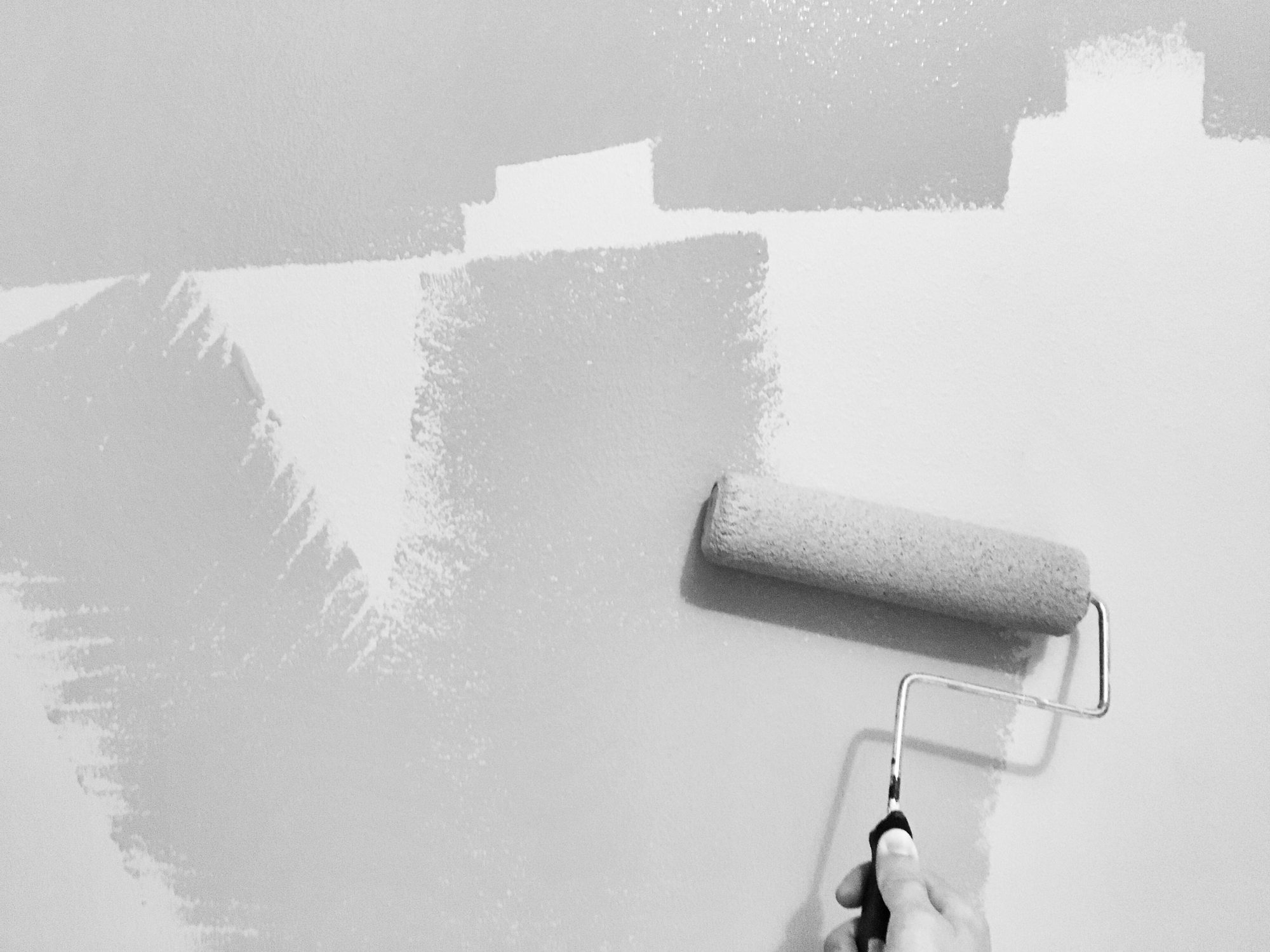 Rolo passando tinta branca sobre uma parede cinza, com as faixas da primeira demão